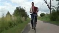 JEDZIE NA ROWERZE I GRA NA AKORDEONIE.